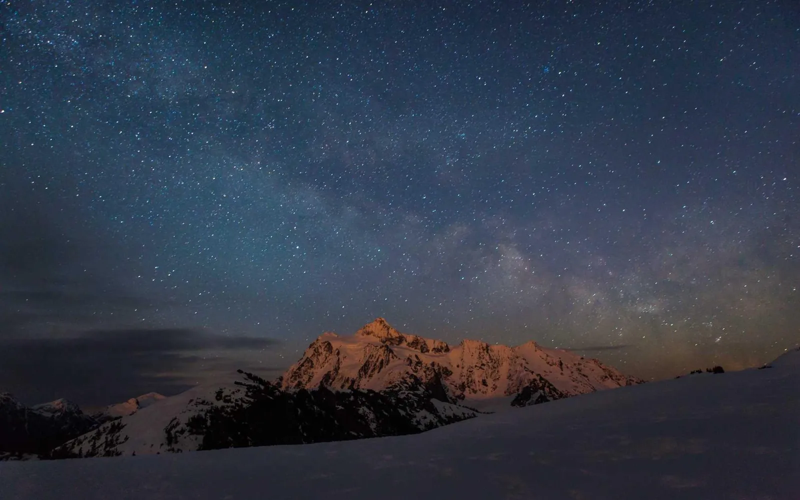 Céu estrelado sobre uma montanha nevada, com o pico iluminado
